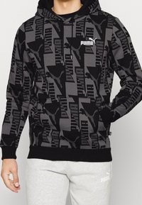 Sweat à capuche noir et gris avec des motifs géométriques, logo Puma, capuche à cordon de serrage, poignets et ourlet côtelés. Tissu à texture douce.