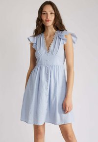 Robe bleu clair avec un décolleté en V profond, des manches volantées et une fermeture à boutons sur le devant. Fabriquée en tissu rayé avec une finition texturée.