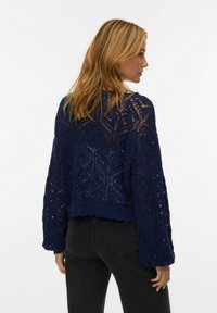 Maglione lavorato a maglia blu navy caratterizzato da intricati motivi in pizzo, maniche lunghe e orlo corto. I bordi scallop completano il design.