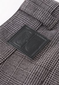 Gray patterned fabric with vertical and horizontal lines, featuring a black leather patch with embossed design. Textured surface, flat design.
