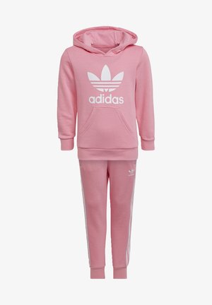 Tuta Adidas rosa composto da una felpa con cappuccio e tasca a marsupio con logo bianco, abbinato a pantaloni coordinati con righe laterali bianche.