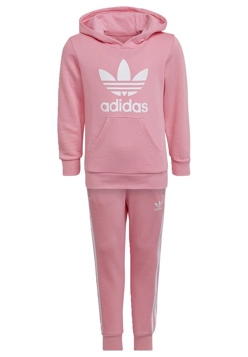 Tuta Adidas rosa composto da una felpa con cappuccio e tasca a marsupio con logo bianco, abbinato a pantaloni coordinati con righe laterali bianche.