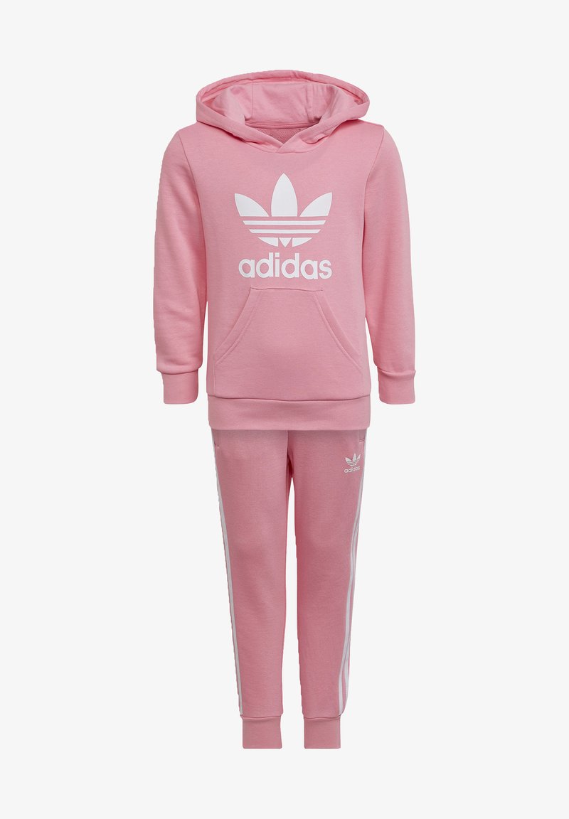 Tuta Adidas rosa composto da una felpa con cappuccio e tasca a marsupio con logo bianco, abbinato a pantaloni coordinati con righe laterali bianche.