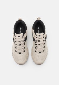 Beżowe i czarne buty sportowe z siateczkową cholewką, teksturowaną podeszwą, sznurowadłami i logo na języku. Posiadają kontrastową opaskę w innym kolorze.