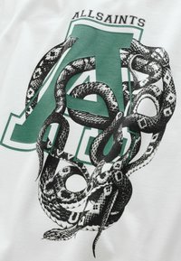 Valge puuvillane T-särk, millel on musta ja halli värvi madu kujutis, mis on põimunud rohelise tähe "A" ümber, ning tekst "ALLSAINTS" selle kohal.