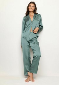 Satin slaapset in gedempt groen, bestaande uit een knoopshirt met kraag en losse, elastische broek met tailleband. Glad oppervlak overal.