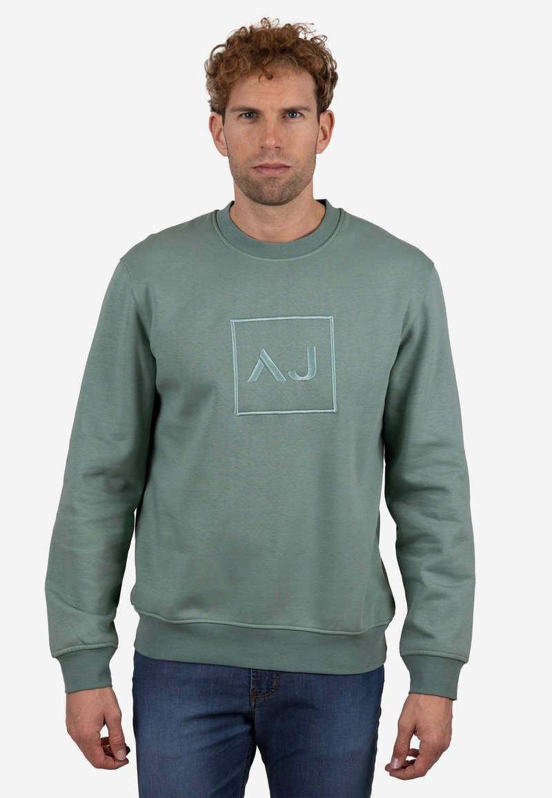 Sudadera de algodón verde con cuello redondo, puños y cinturilla acanalados. Cuenta con un logotipo cuadrado cosido en azul claro.