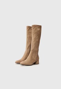 Bottes en suède beige jusqu'aux genoux avec un bout carré et un talon bloc. Caractéristiques d'une fermeture éclair à l'avant et d'accents cousus sur le côté. Texture lisse sur toute la surface.