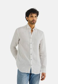 Leichte, langärmlige weiße Leinenbluse mit spitzem Kragen, Knopfleiste vorn und blauen Knöpfen, kombiniert mit blauen Denim-Jeans.