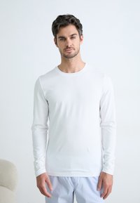 Cămașă albă cu mânecă lungă, confecționată dintr-un material fin și ușor, cu o guler rotund. Este purtată cu pantaloni de pijama cu dungi.