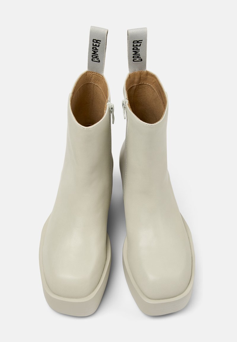 Vita läderankelboots med en slät yta, fyrkantiga tår och tjocka gummisulor. Har en sidodragkedja och en dragflik med "CAMPR"-bokstäver.