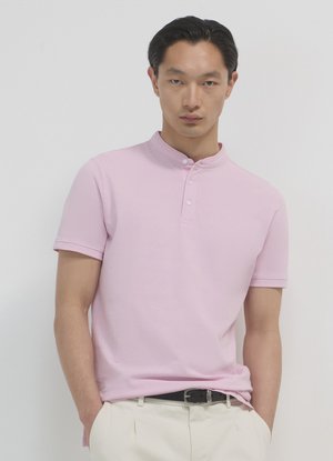 Polo a maniche corte di un rosa pallido con colletto alla coreana, dotato di patta con bottoni e realizzato in un tessuto morbido simile al cotone.