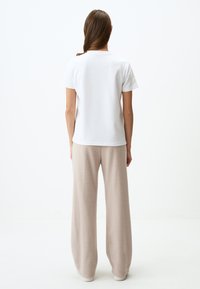 T-shirt bianca in cotone con maniche corte, abbinata a pantaloni ampi beige chiaro realizzati in un tessuto morbido e texturizzato. Colori semplici e neutri.