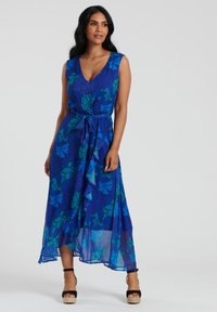 Maxiklänning i blått med blommönster, med V-ringning, figursydd liv och en flödande nederdel. Bältes runt midjan med volangdetaljer.
