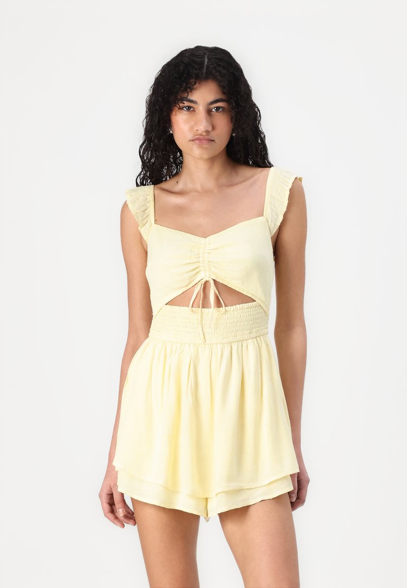 Conjunto de dos piezas en color amarillo con tirantes acampanados, cuerpo fruncido, detalle recortado y cintura fruncida; tejido ligero y fluido, con parte inferior corta.