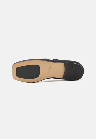 Zapato de ante negro con una suela sólida y suave. Presenta una puntera redondeada y dos hebillas metálicas en la parte superior, con un acento de goma texturizada.