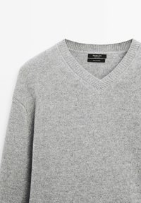 Grauer Kaschmirpullover mit V-Ausschnitt und geripptem Kragen. Weiche Textur und feines Strickmuster. Das Etikett trägt die Aufschrift "Massimo Dutti, 100% Kaschmir."