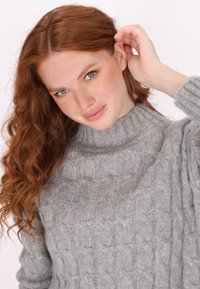 Pull en maille torsadée gris clair avec un col montant. Fabriqué en laine douce, il présente un motif texturé et des poignets côtelés. Design ajusté.