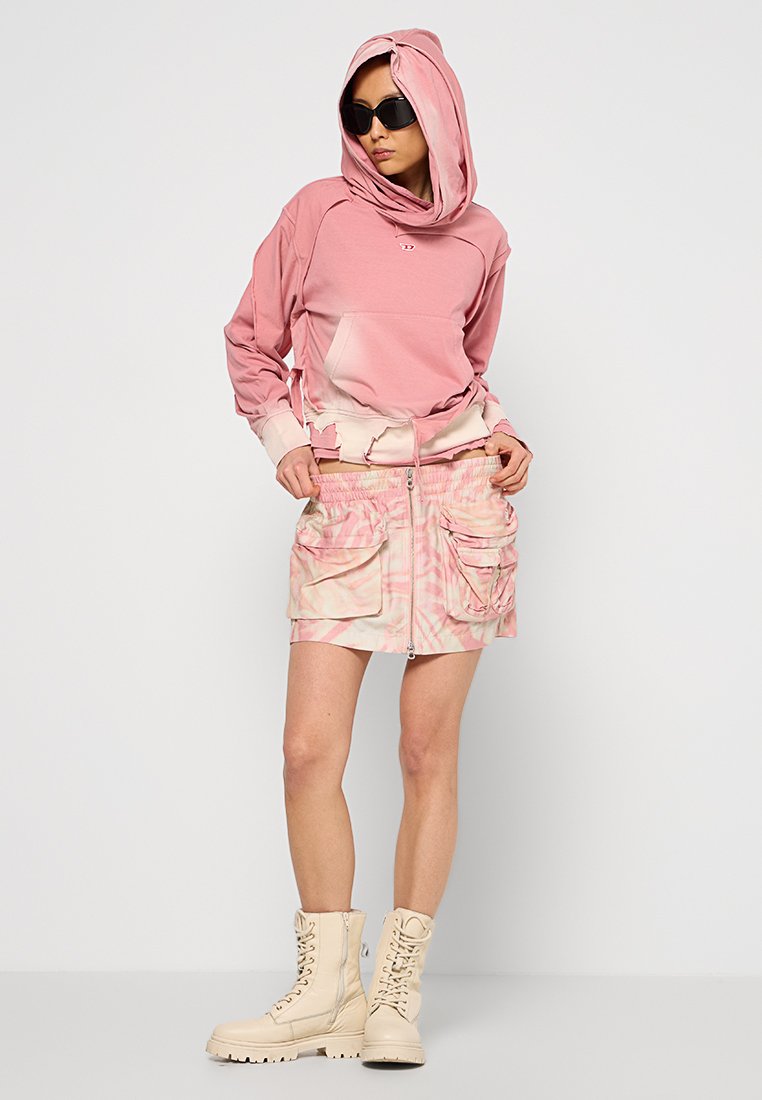 Rosa Kapuzenpullover mit großer Kapuze und Kängurutasche, kombiniert mit einem hellrosa Batik-Minirock mit Cargo-Taschen und Reißverschluss. Tanfarbene Kampfstiefel.