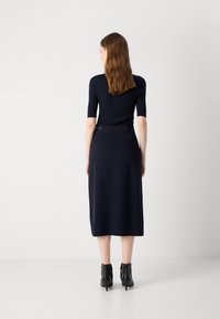 Top en tricot côtelé bleu marine à manches courtes associé à une jupe bleu marine de longueur genou. La jupe présente un détail de bouton au niveau de la taille. Bottines noires au niveau des chevilles.