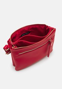 Borsa in pelle rossa con hardware dorato, dotata di chiusura con zip e due scomparti interni. Texture liscia con tasca laterale con zip.