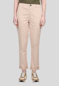 Pantalons en mélange de coton beige clair avec une coupe droite, jupes retournées, fermeture à bouton et poches avant, associés à des baskets marron et blanches.