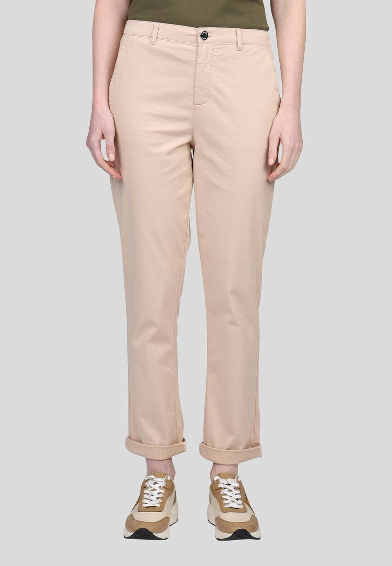 Pantalons en mélange de coton beige clair avec une coupe droite, jupes retournées, fermeture à bouton et poches avant, associés à des baskets marron et blanches.