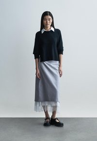 Mustast kudumist kampsun, hall midi seelik pitsäärisega ja mustad kingad. Komplekti iseloomustab kihiline välimus kontrastsete tekstuuridega.