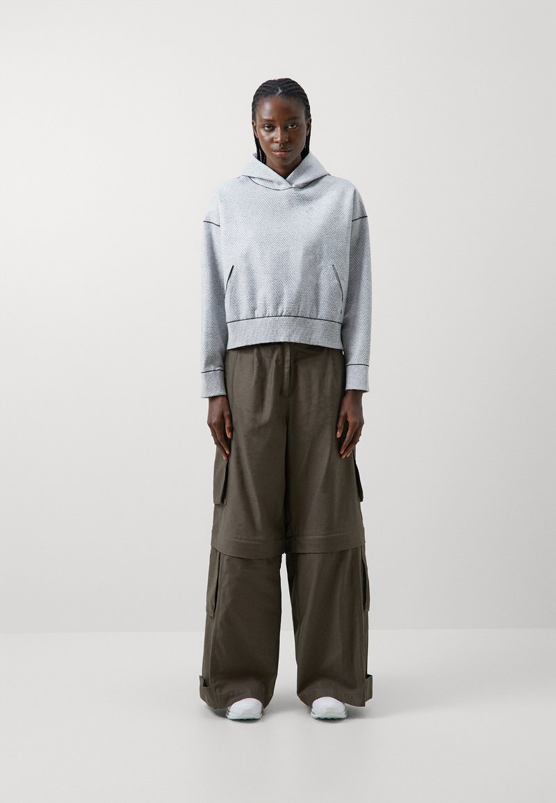 Grauer Kapuzenpullover mit strukturiertem Muster und elastischen Bündchen, kombiniert mit locker sitzenden, olivgrünen Cargo-Hosen und weißen Sneakern.