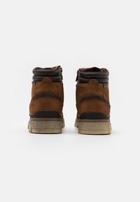 Botas de tobillo de ante marrón con detalles en cuero oscuro, forma redondeada y cuello acolchado. Cuenta con una suela texturizada y cremallera en la parte posterior.