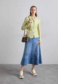 Cardigan côtelé vert clair avec fermeture à boutons, jupe en denim forme A et baskets blanches avec des accents dorés. Petit sac à main marron avec une bandoulière.