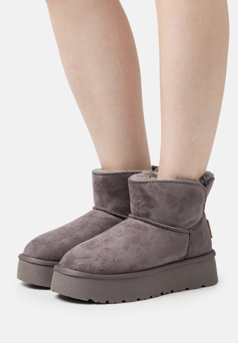Botas de tobillo de ante gris con forro de felpa, punta redondeada y suela de plataforma baja. Presentan un puño flexible y un sutil detalle de costura.