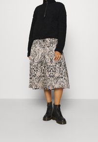 Zwarte, textuur fleece top met een ritssluiting bij de kraag; gecombineerd met een roze en zwarte paisley-gepatenteerde rok; zwarte veterschoenen met een chunky zool.