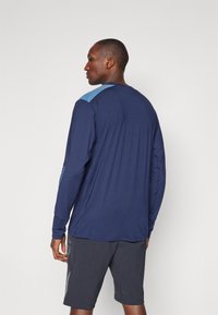 Langarm sportshirt in marineblauw met lichtblauwe schouderaccenten, met een soepele textuur en stijlvolle stiksels, gedragen met grijze shorts.
