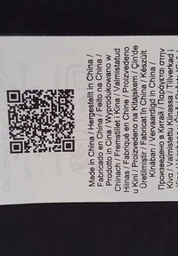 Etikett mit gedrucktem Text in mehreren Sprachen, mit einem QR-Code und einem weißen Hintergrund. Enthält Informationen über die Herkunft des Produkts.