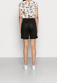 Svarta skräddarsydda shorts med uppvikt kant, bärs tillsammans med en blommig blus. Modellen står med ryggen mot kameran, i sällskap med vita sneakers. Enkla bakgrund.