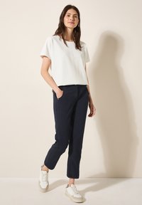 Haut court à manches courtes texturé blanc, pantalon slim-fit bleu marine et baskets blanches. Le pantalon présente des poches latérales et un détail de couture subtil.