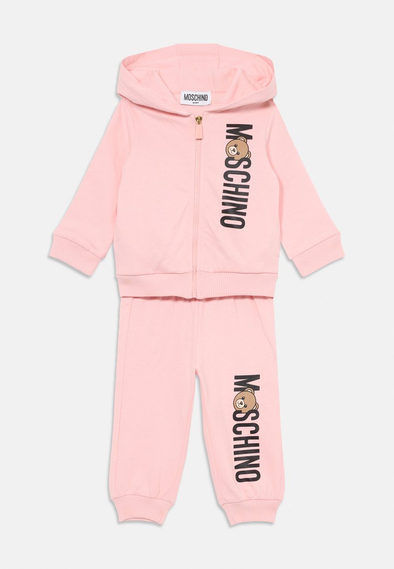 Ensemble de survêtement pour bébé Moschino rose, comprenant un hoodie zippé et un jogger assorti. Logo noir et graphique d'ours en cartoon sur le devant. Matière douce, poignets côtelés.