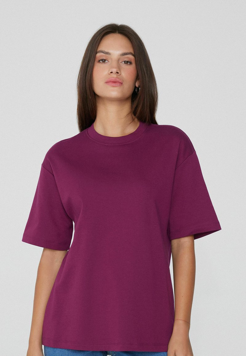Camiseta de manga corta en algodón morado intenso, con un cuello redondo y un corte holgado. Textura suave sin patrones ni acentos visibles.