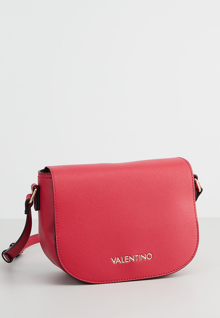 Sac bandoulière en cuir rouge avec un rabat courbé, détail du logo doré et sangle réglable. Texture lisse avec des éléments de design minimalistes.