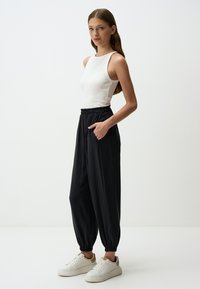 Top a canotta bianco a coste con pantaloni tapered neri a vita elastica. Le sneaker sono bianche con accenti color sabbia. Tessuto liscio, vestibilità comoda.