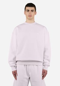 Light pink crewneck sweatshirt with ribbed cuffs, matching elastic waistband, and subtle branding on the chest. Soft fabric texture.