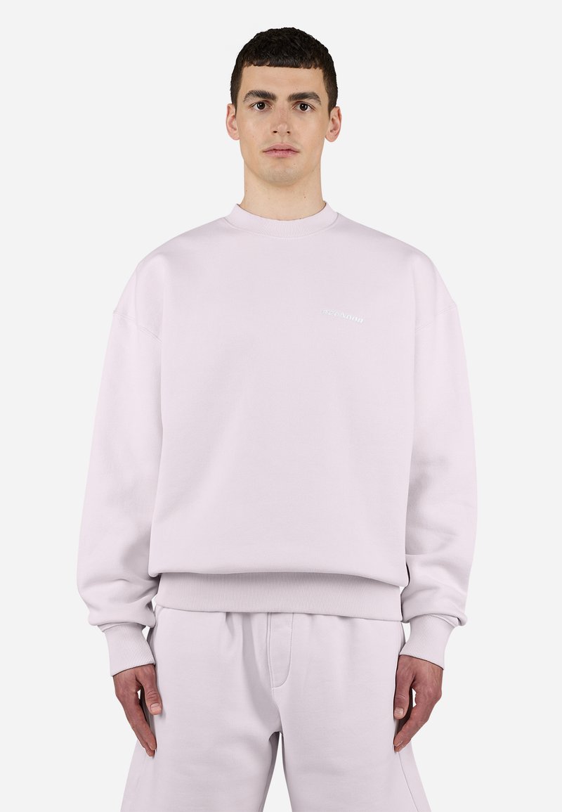 Light pink crewneck sweatshirt with ribbed cuffs, matching elastic waistband, and subtle branding on the chest. Soft fabric texture.