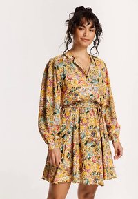 Blommig klänning i gult, med långa ärmar, krage och elastisk midja med en samlad kjol.