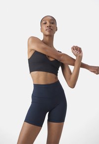 Svart sportbh med rundad halsringning, kombinerad med högmidjade marinblå shorts. Tyget verkar slätt och åtsittande med minimala sömmar.