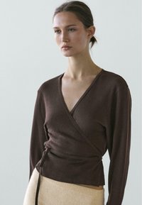 Brun omslagsweater med lange ærmer, blød tekstur og V-hals, kombineret med en cremefarvet strikket nederdel med ribbet talje.