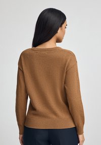 Brauner gestrickter Pullover mit Rundhalsausschnitt, geripptem Saum und langen Ärmeln, von hinten gezeigt, mit weicher Textur und lockerer Passform.