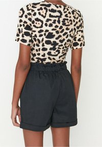 T-shirt w panterkę wykonany z miękkiego materiału z krótkimi rękawami, zestawiony z czarnymi szortami z wysokim stanem z marszczoną talią.