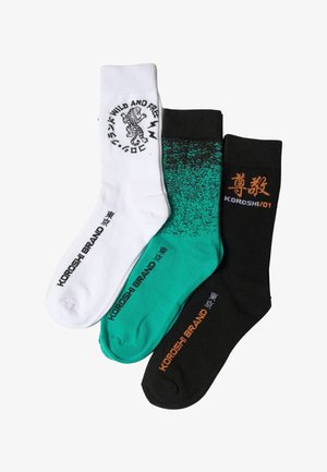 Tres pares de calcetines deportivos en blanco, verde azulado con motas negras y negro, cada uno con el texto de la marca Koroshi y caracteres japoneses.