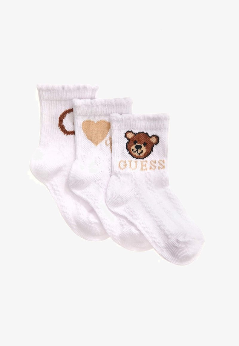Trois chaussettes blanches pour bébé avec des motifs tricotés, comportant un visage d'ours et le texte "GUESS" sur l'une, un cœur sur une autre, et un cercle partiel sur la dernière.